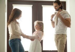 Caring mother helping little daughter dressing for walk with dad, family talking getting ready to go out standing in house hall, divorced young couple shared parenting and joint custody concept